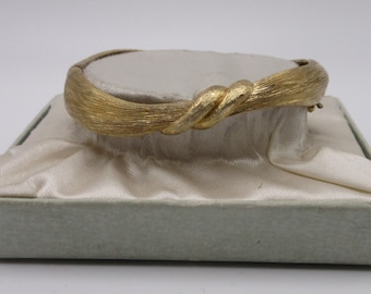 Peut inclure: Un bracelet jonc doré avec un design torsadé. Le bracelet est présenté sur un coussin de satin blanc dans une boîte bleu clair.