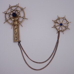 May include: A pair of gold-tone brooches with blue and clear rhinestones. The brooches are connected by a gold chain.
