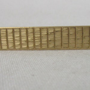 May include: A gold-toned tie bar with a textured, geometric design.