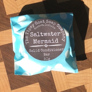 May include: A blue and white polka dot package containing a round bar of soap. The soap is labeled "The Tipsy Goat Soap Company, Warsaw, Indiana" and "Saltwater Mermaid Solid Conditioner Bar 50g".
