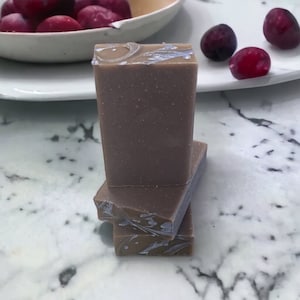 May include: A stack of three brown and purple soap bars with a swirl design. The soap bars are on a white marble surface.