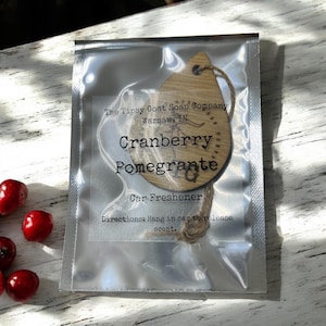 May include: A wooden car freshener in a clear plastic package. The freshener is teardrop-shaped with the words "Cranberry Pomegrante" printed on it. The package also includes the text "Car Freshener" and "Directions: Hang in car to release scent."