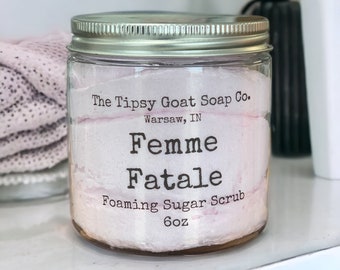 Op de afbeelding: Een glazen pot met een zilveren deksel gevuld met een roze schuimende suiker scrub. Het etiket vermeldt "The Tipsy Goat Soap Co. Warsaw, IN Femme Fatale Foaming Sugar Scrub 6oz"