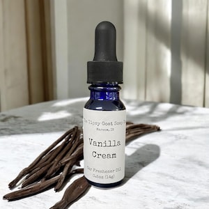 May include: A small blue glass bottle with a black dropper top. The bottle is labeled "Tipsy Goat Soap Co. Warsaw, IN" and "Vanilla Cream Car Freshener Oil 0.5oz (14g)".