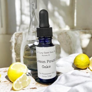 May include: A blue glass bottle with a black dropper top and a white label that reads "The Tipsy Goat Soap Co. Warsaw, IN Lemon Pound Cake Car Freshener Oil 0.5oz (14g)".