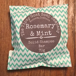 May include: A white and green chevron patterned pouch with a brown circle label that reads "The Tipsy Goat Soap Company, Warsaw, Indiana, Rosemary & Mint, Solid Shampoo Bar, 70g"