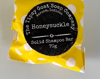 May include: A yellow polka dot package with a black label that reads "The Tipsy Goat Soap Company, Warsaw, Indiana" and "Honeysuckle Solid Shampoo Bar 70g".