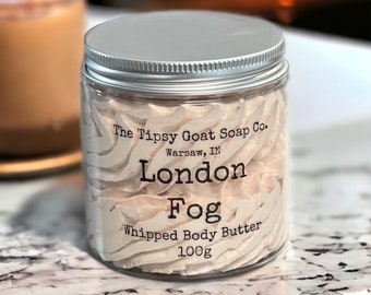 Pode incluir: Um frasco de vidro com tampa prateada cheio de manteiga corporal batida de cor marrom claro. O frasco tem um rótulo que diz "The Tipsy Goat Soap Co. Warsaw, IN London Fog Whipped Body Butter 100g".