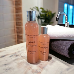 May include: Two bottles of pink body wash with a silver cap. The bottles are labeled "Love Potion" and "Tipsy Goat Soap Company, Warsaw, IN". The larger bottle is 8 oz and the smaller bottle is 4 oz.