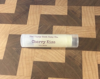 Op de afbeelding: Een witte tube lippenbalsem met de tekst "The Tipsy Goat Soap Co. Cherry Kiss Lip Balm" erop gedrukt.
