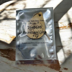 May include: A wooden car air freshener with the text "The Tipsy Goat Soap Company Warsaw, IN Toasted Marshmallow TG Car Freshener Directions: Hang in car to release scent."