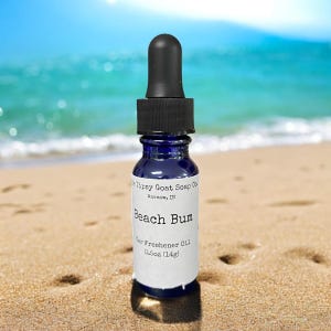 May include: A small blue glass bottle with a black dropper top. The bottle is labeled "Tipsy Goat Soap Co. Warsaw, IN Beach Bum Car Freshener Oil 0.5oz (14g)"