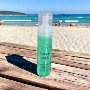May include: A clear plastic bottle of foaming hand soap with a green liquid inside. The bottle has a label that says "The Tipsy Goat Soap Company, Narrows, IL" and "Sand & Surf Foaming Hand Soap 7.5oz".