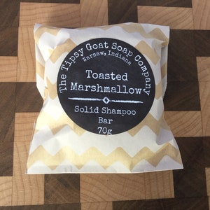 May include: A white paper bag with a chevron pattern and a black and white label that reads "The Tipsy Goat Soap Company, Warsaw, Indiana, Toasted Marshmallow, Solid Shampoo Bar, 70g."