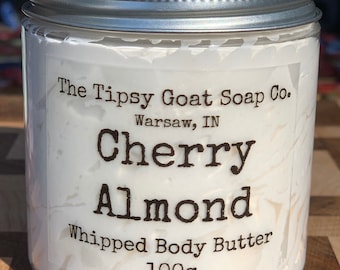 May include: A white jar with a silver lid containing Cherry Almond Whipped Body Butter. The jar is labeled "The Tipsy Goat Soap Co. Warsaw, IN" and "100g".