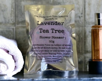 May include: A purple and white shower steamer with the text "Lavender Tea Tree Shower Steamer 50g" on a silver foil package. The package also includes directions and ingredients for the shower steamer.