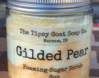 Op de afbeelding: Een glazen pot met een zilveren deksel gevuld met een lichtgroene en bruine suiker scrub. Het etiket luidt "The Tipsy Goat Soap Co. Warsaw, IN Gilded Pear Foaming Sugar Scrub 6oz"