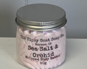 Pode incluir: Um frasco transparente com tampa prateada cheio de manteiga corporal batida rosa. O rótulo diz "The Tipsy Goat Soap Co. Warsaw, IN Sea Salt & Orchid Whipped Body Butter 50g".