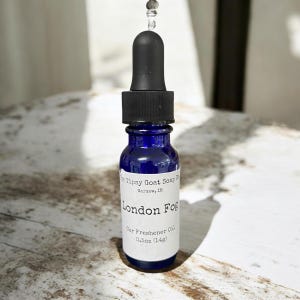 May include: A small blue glass bottle with a black dropper top. The bottle is labeled "Tipsy Goat Soap Co. Warsaw, IN London Fog Car Freshener Oil 0.5oz (14g)"