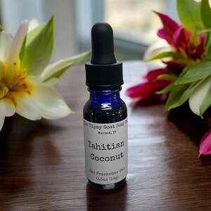 May include: A small blue glass bottle with a black dropper top. The bottle is labeled "The Tipsy Goat Soap Co. Warsaw, IN" and "Tahitian Coconut Car Freshener Oil 0.5oz (14g)"