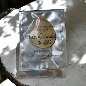May include: A wooden car air freshener in the shape of a teardrop with the text "The Tipsy Goat Soap Company Warsaw, IN Lemon Pound Cake G Car Freshener Directions: Hang in car to release scent."