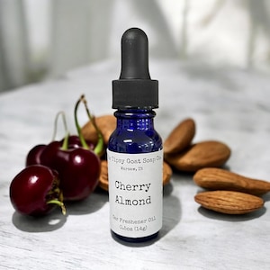 May include: A small blue glass bottle with a black dropper top. The bottle is labeled "Tipsy Goat Soap Co. Warsaw, IN" and "Cherry Almond Car Freshener Oil 0.5oz (14g)".
