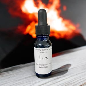 May include: A small blue glass bottle with a black dropper top. The bottle is labeled "The Tipsy Goat Soap Co. Warsaw, IN" and "Lava Car Freshener Oil 0.5oz (14g)"