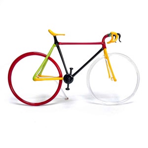 May include: A glass sculpture of a bicycle with red, black, yellow, and green glass. The bicycle is on a white background.