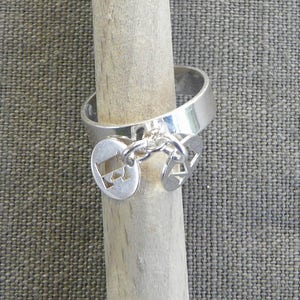 Peut inclure: Une bague en argent avec une chaîne et trois breloques. Les breloques sont rondes et ont des motifs découpés. La bague est sur une surface en bois.