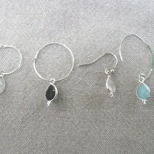 Puede incluir: Cuatro pares de pendientes de aro de plata con gotas de piedras preciosas. Los pendientes presentan una variedad de piedras preciosas, incluyendo blanco, negro y azul.