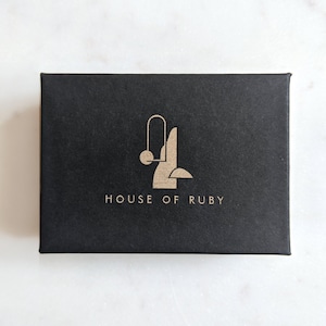 May include: Black box with a gold logo that says "HOUSE OF RUBY". The logo is a stylized abstract design with a circle and lines.