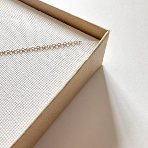 May include: A gold chain necklace in a brown cardboard box with a white interior.