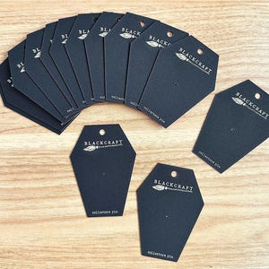 May include: A stack of black card stock earring display cards with a white logo and text that reads "BLACKCRAFT" and "collectors pin".