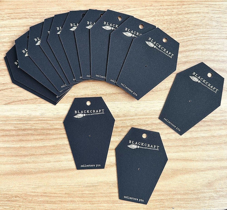 May include: A stack of black card stock earring display cards with a white logo and text that reads "BLACKCRAFT" and "collectors pin".