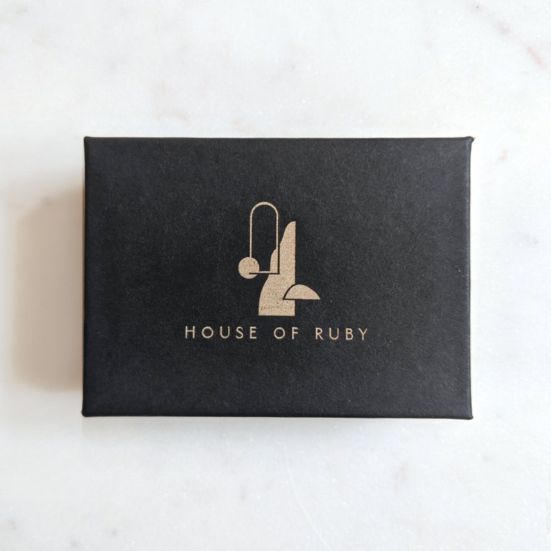 May include: Black box with a gold logo that says "HOUSE OF RUBY". The logo is a stylized abstract design with a circle and lines.