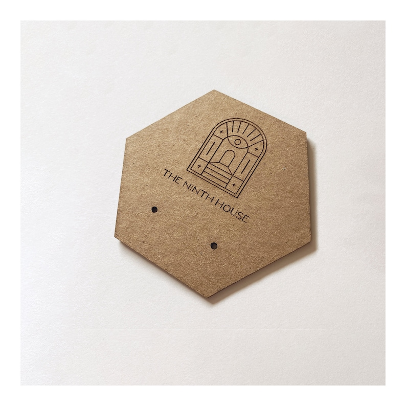May include: A hexagonal brown cardboard tag with two holes. The tag features a line drawing of an arched doorway with an eye inside and the text "THE NINTH HOUSE".