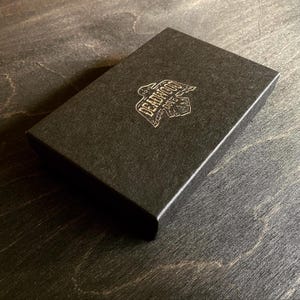 May include: Black box with a gold logo that says "Deadwood Dice".
