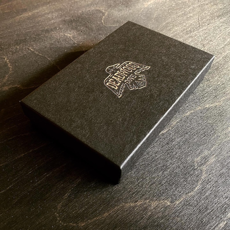 May include: Black box with a gold logo that says "Deadwood Dice".