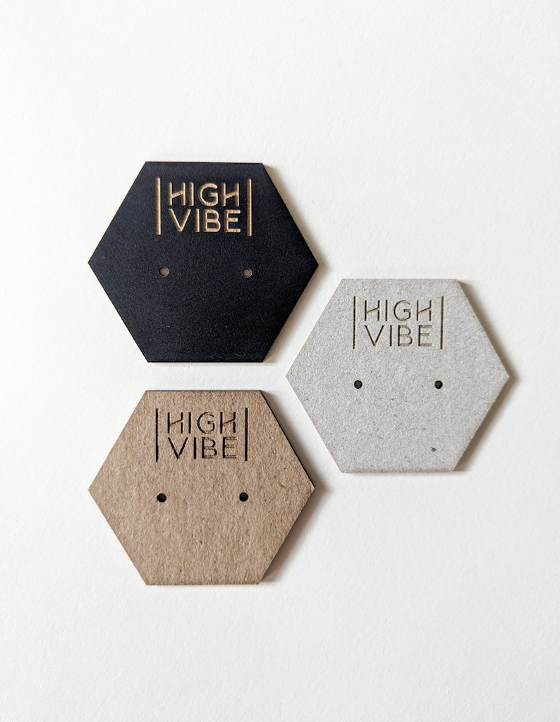May include: Three hexagonal earring display cards with the text "HIGH VIBE" printed on them. The cards are black, gray, and brown.