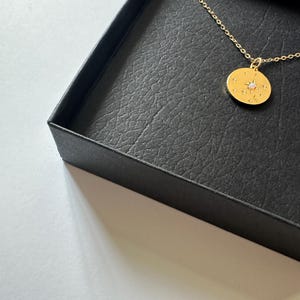 May include: A gold necklace with a round pendant featuring a small white stone surrounded by smaller stones. The pendant is in a black jewelry box.