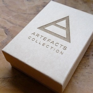 Peut inclure: Une bo&icirc;te blanche avec un logo triangulaire brun et le texte "ARTEFACTS COLLECTION" imprim&eacute; sur le devant.
