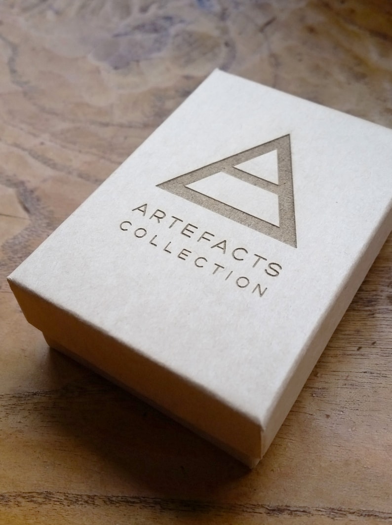 Peut inclure: Une bo&icirc;te blanche avec un logo triangulaire brun et le texte "ARTEFACTS COLLECTION" imprim&eacute; sur le devant.