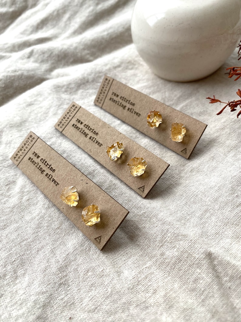 May include: Three pairs of raw citrine earrings on brown cards with the text "raw citrine sterling silver" and the letter "A" printed on each card.