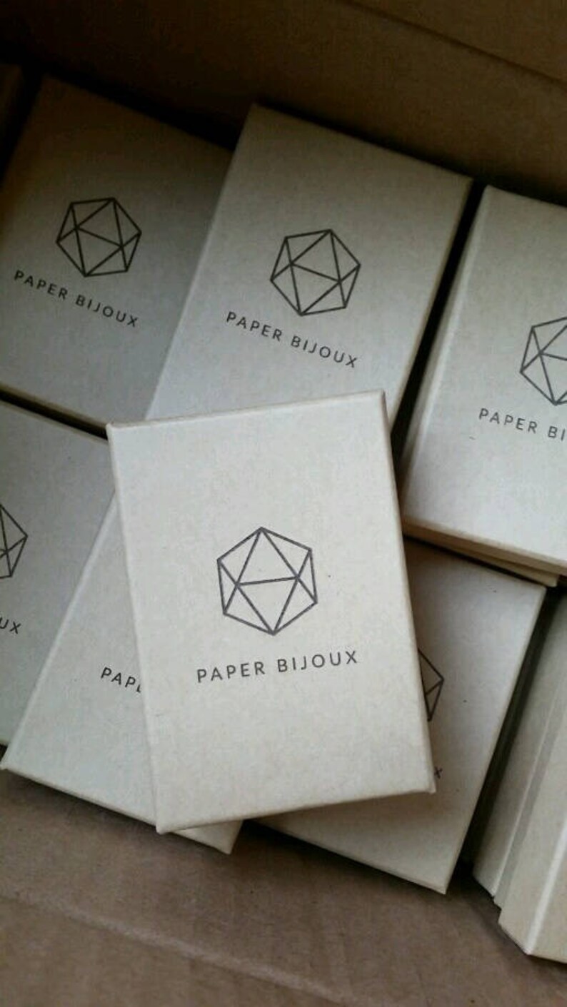 Peut inclure: Une pile de petites bo&icirc;tes en carton brun avec un motif g&eacute;om&eacute;trique et le texte "PAPER BIJOUX" imprim&eacute; sur chaque bo&icirc;te.