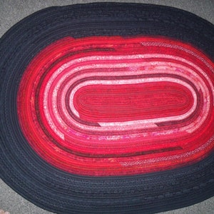 May include: A red and black oval rug with a concentric circle design. The rug is made of fabric strips sewn together.