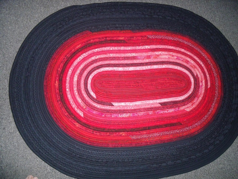 May include: A red and black oval rug with a concentric circle design. The rug is made of fabric strips sewn together.
