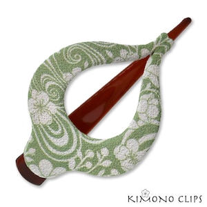 May include: A green and white floral patterned hair clip with a brown wooden stick. The clip is shaped like a teardrop and has a loop in the middle.