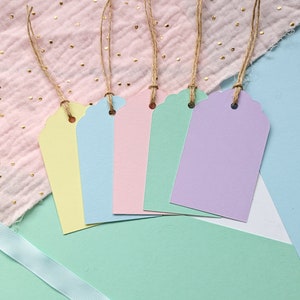 May include: Five pastel-coloured gift tags with scalloped edges and twine string. The tags are yellow, light blue, pink, light green, and lavender.