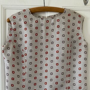 May include: A sleeveless blouse with a white background and a geometric pattern of red and grey squares.