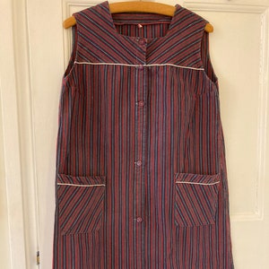May include: A long, sleeveless dress with a button-up front and two pockets. The dress is made of a striped fabric in shades of red, black, and white.